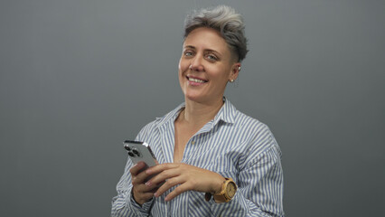 Woman in striped shirt wearing wooden wristwatch tapping fingers on smartphone screen in grey...