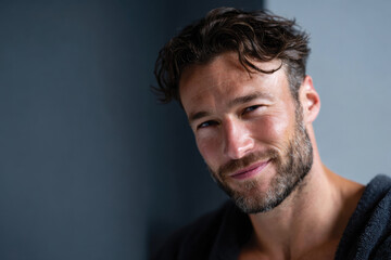 Fototapeta premium A confident man in a bathrobe is smiling at the camera, exuding warmth and approachability, embodying self-assurance and happiness in a casual setting.