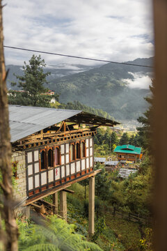 View of a traditional Bhutanese house standing on stilts, overlooking a valley with mist-shrouded mountains, a blend of cultural and natural elements, Jakar, Bhutan.
