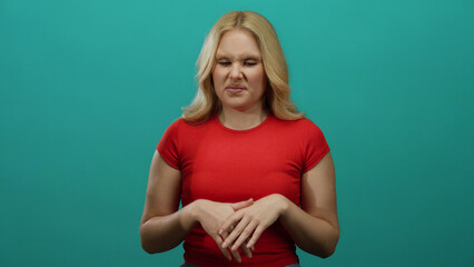 Woman in red shirt with blonde hair stands against blue background expressing confusion and...