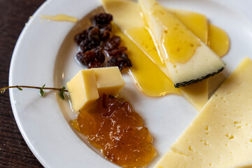 Assorted cheeses on a plate with honey, raisins, and orange marmalade