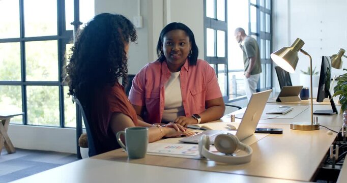 African American women coworkers using charts, pointing at laptop and typing to finalize plan