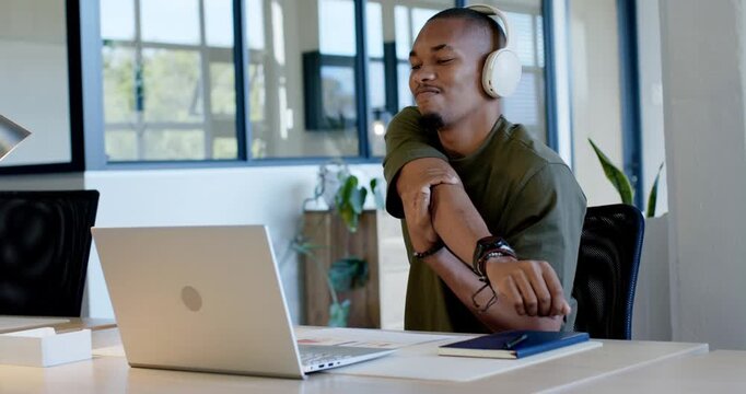 African man in olive tee sitting at desk checking laptop adjusting wrist stretching arm easing pain
