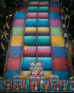 View of a vibrant, rainbow-colored staircase ascending towards a Hindu temple, with devotees gathered at the base, a burst of culture, Kuala Lumpur, Malaysia.