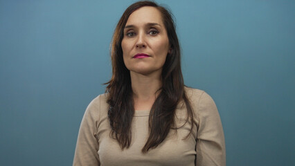 Obraz premium Woman standing against a blue wall, expressing calmness and confidence, highlighted by her neutral attire and thoughtful gaze.