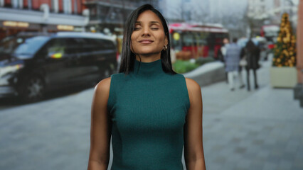 Woman smiling on busy urban street with blurred background, wearing green, showcasing vibrant city life and cultural diversity.
