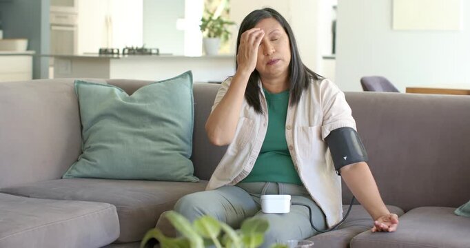 Mature woman in green top sitting on sofa, cuff inflating, checking BP monitor after feeling faint
