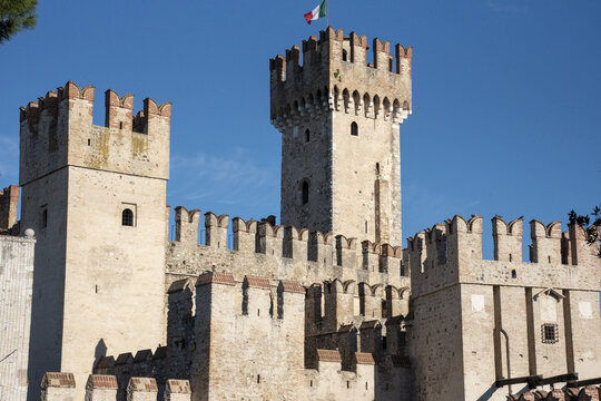 View of the imposing Scaliger Castle, with its crenellated walls and towers under a clear blue sky, casting long shadows, Sirmione, Lombardy, Italy.