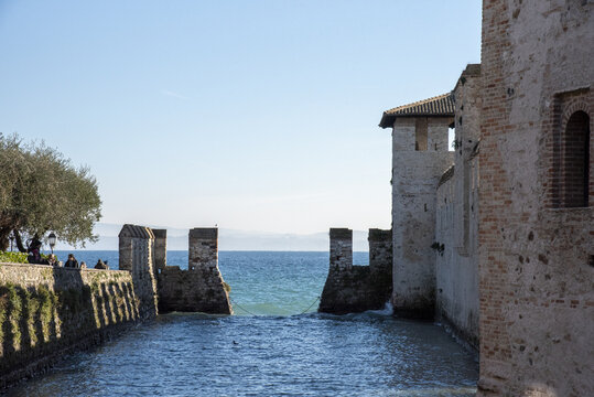 View of ancient stone walls embrace the shimmering turquoise waters, creating a striking contrast of textures and colors, Sirmione, Lombardy, Italy.