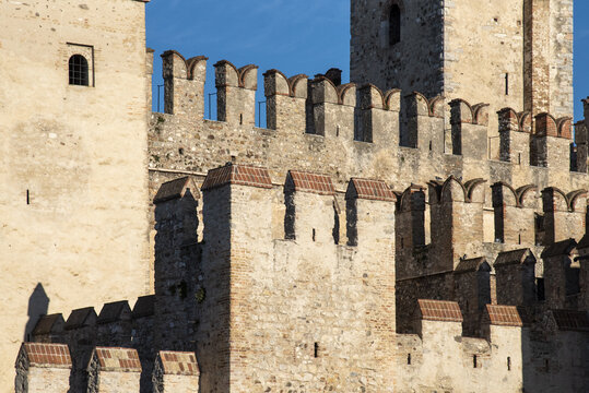 View of textured ancient stone walls with crenellations under a clear blue sky, showcasing the enduring architecture, Sirmione, Lombardy, Italy.