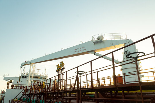 Industrial deck crane on an oil tanker ship captured in golden hour. Visible SWL lifting marks. Maritime engineering and offshore transport.