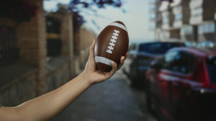 Man holding football on city street with cars and buildings in the background, showcasing a sporting theme in an urban environment with a focus on leisure and sports.