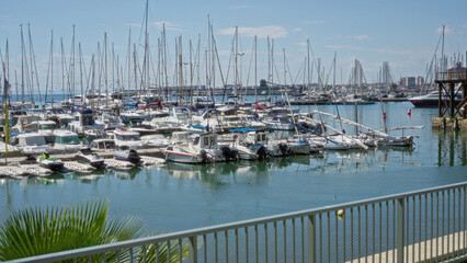 Sailboats docked in a sunny marina in torrevieja with a view of the calm sea, vibrant sky, and wooden pier in alicante, spain, showcasing a serene outdoor seascape.