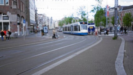 Obraz premium Blurred street scene in an amsterdam cityscape with tram and pedestrians in out-of-focus background for urban travel settings.