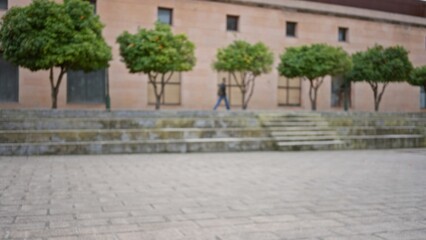 Blurred view of man walking past trees on a university campus with defocused background and bokeh effect highlighting the old building and stone steps in focus.
