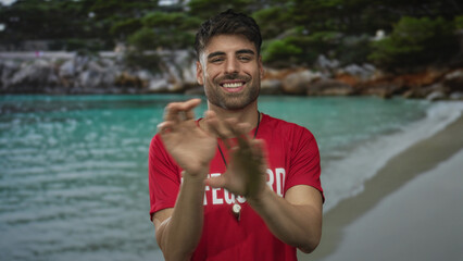 Hispanic lifeguard man claps hands wearing red shirt and whistle on tropical beach under bright...