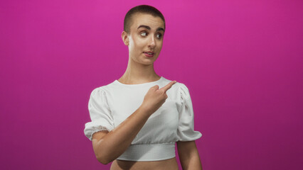 Obraz premium Young woman with short hair in white crop top shows both middle fingers to camera in a pink photo studio, grimacing and shrugging shoulders; defiance attitude.