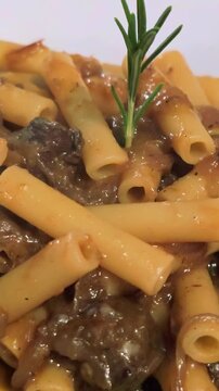 Steaming hot plate of zita tagliata pasta with a traditional beef and onion Genovese sauce, an authentic dish from Naples, garnished with a sprig of fresh rosemary on a white background