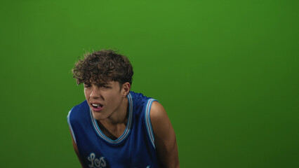 Teenage boy mouth grimace leaning forward in studio wearing blue basketball jersey; strain effort...