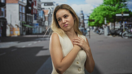 Woman clasping hands to chest on a busy city street with closed eyes and gentle tilt of head, wearing sleeveless vest; serenity.