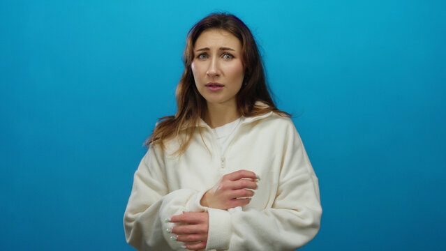 Young woman standing isolated against a vibrant blue background wearing a white sweater, showcasing a thoughtful expression and natural hair flowing freely.
