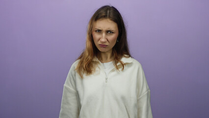 Fototapeta premium Woman frowning in front of an isolated purple background wearing a white sweatshirt, expressing displeasure with a serious expression in a studio setting.