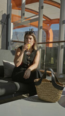 Fototapeta premium Woman holding a glass of orange juice on a cruise terrace with straw bag and sunglasses on head; relaxed vacation.