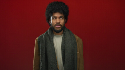 Man with curly hair and beard wearing scarf and jacket stands against vibrant red wall looking upwards in contemplation © Krakenimages.com