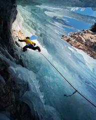 Man climbing frozen ice wall at winter mountains