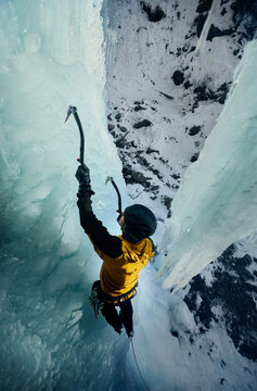 Man climbing frozen ice wall at winter mountains