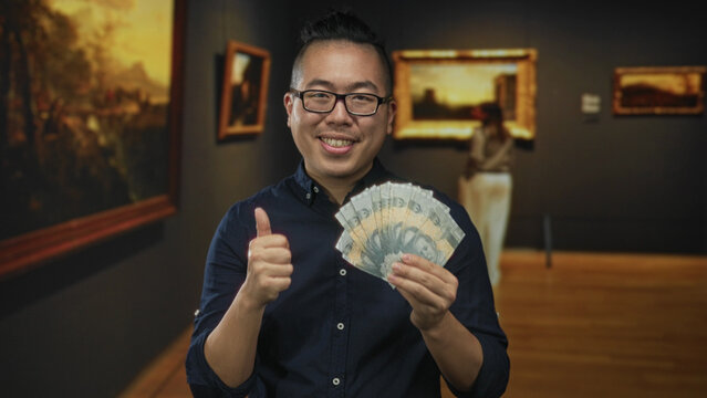 Man holding a fan of rupiah banknotes and gives thumbs up while smiling in museum building; wealth prosperity joy.