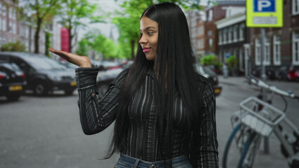Obraz premium Young woman standing wearing black striped shirt and blue jeans holds palms up on city street in daylight; uncertainty.