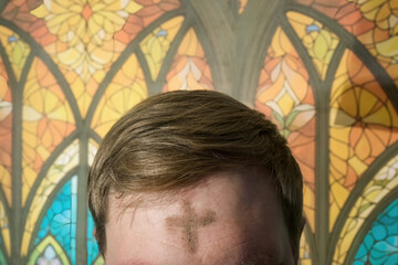 Man's forehead with ash wednesday cross against stained glass