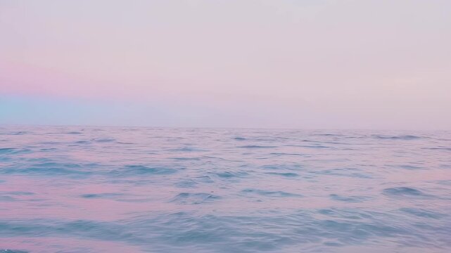 Gentle ocean waves reflect soft pink and purple hues under a serene sky