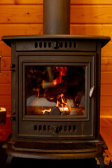 An old-fashioned stove burns wood, heats a country house. A wood-burning stove with a burning fire in the interior and stacked logs on an open background 