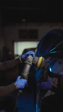 Cinematic close up of a professional detailer polishing a car body with an electric orbital buffer inside an auto detailing studio. Automotive paint correction and car care concept