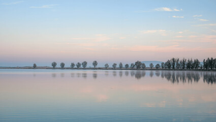 Calm lake with smooth water reflections and distant trees in early morning light