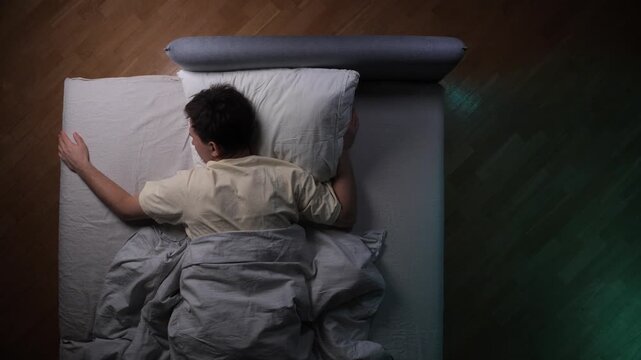 Man lying sleepless in bed trying to ignore smartphone in the dark bedroom, illustrating themes of insomnia, sleep deprivation, screen addiction, and night time digital device use