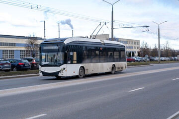 Obraz premium Modern Electric Trolleybus Driving on Urban Street with Overhead Power Lines and Industrial Buildings