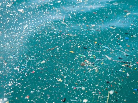A wide view of water filled with countless tiny plastic particles and debris, showing microplastic pollution dispersed across the surface and beneath the water.