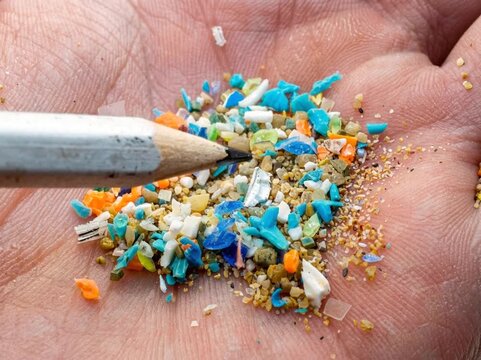 A close-up of a human hand holding colorful microplastic fragments and sand, highlighting the scale and visibility of plastic pollution at a granular level.