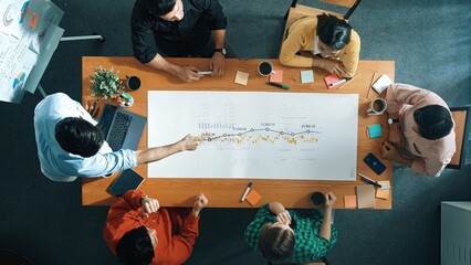 A diverse team engages in an important meeting, analyzing charts and discussing strategies. The modern office setting emphasizes collaboration and creativity among professionals. Raster