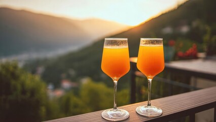 Obraz premium Two orange drinks in wine glasses on a balcony at sunset with a mountain view. Concept Sunset balcony cocktails with mountain view, Orange drinks in wine glasses