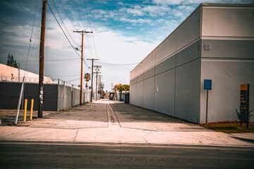 Fototapeta premium Industrial alleyway with power lines and large warehouse building under a cloudy sky