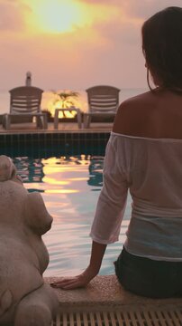 Woman sit near pool, enjoy spectacular sunset view over ocean horizon. Palm trees and sunbeds, luxury tropical resort in Thailand, Koh Phangan island. Travel, tourism, summer holiday, nature landscape