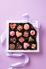 Assorted gourmet chocolates in gift box with ribbon, pink background