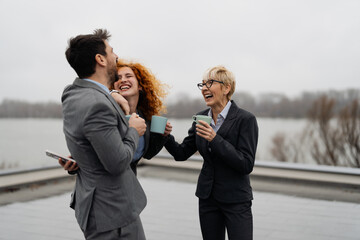 Naklejka premium Group of diverse business colleagues enjoying a coffee break on a modern office rooftop garden with a city skyline view.