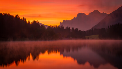 Fototapeta premium A dramatic sunrise casts a fiery orange reflection over a misty mountain lake