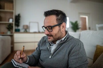 Man writing notes in agenda on couch at home