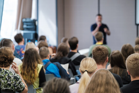 Presenter at front of room engaging crowd during seminar audience listening closely conference setting